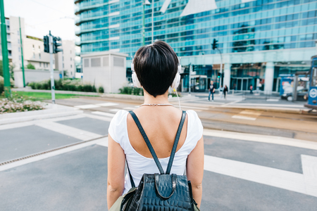 Half length rear view of a caucasian woman with backpack listening music with headphones - music, relax conceptの写真素材