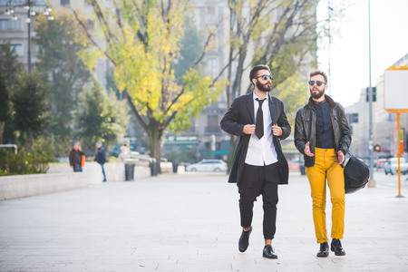 two young bearded blonde and black hair modern businessman, walking in the city backlight, one overlooking right, the other overlooking left - working, successful conceptの写真素材