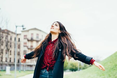 Knee figure of young beautiful caucasian woman feeling free with arms wide open outdoor in the city, smiling - carefree, thoughtless, freedom conceptの写真素材