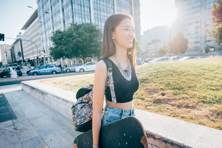 Young woman holding a skateboard and walking outdoors in the cityの写真素材