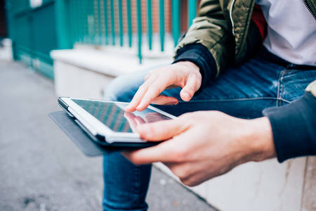 Close up on the hand of young handsome man scrolling and touching the screen of a tablet - technology, social network, communication conceptの写真素材