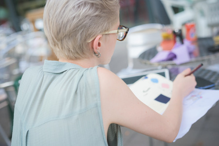 Half length rear view of a young handsome caucasian blonde italian designer sitting in a bar, drawing on her sketchbook, - technology, creativity, working conceptの写真素材