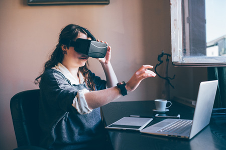 Young handsome caucasian woman using 3D viewer, smart watch, computer and drawing tablet -...