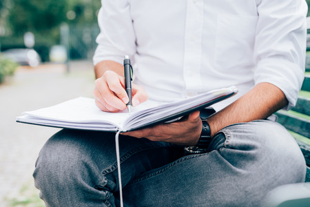 Close up on the hands of a young man writing on his agenda - business, planning, appointment conceptの写真素材