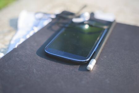 Close up on a smart phone, leaning on a sketchbook, with pencil and earphones beside it - technology, creativity, music conceptの写真素材