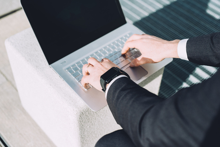 Close up on the hands of businessman tapping the keyboard of a notebook with smartwatch on his wrist - business, working, technologyの写真素材