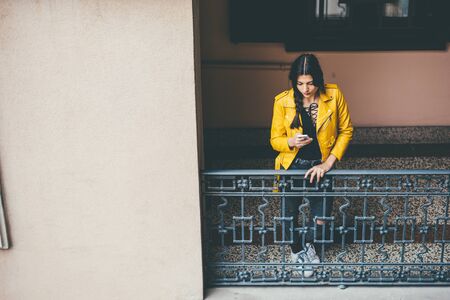 Young beautiful cacuasian brown hair woman leaning on a balcony using smart phone hand hold - technology, social network, communication conceptの写真素材