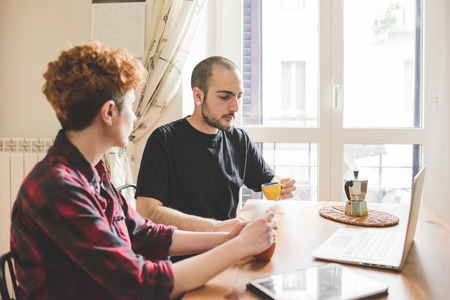 Two young man and woman working indoor in house using computer, talking to each other - work, business, technology conceptの写真素材