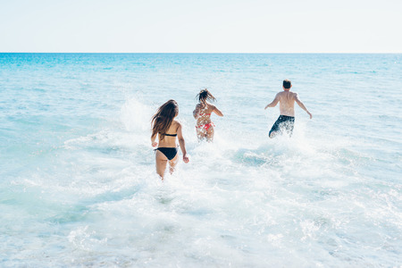 group of young multiethnic friends women and men at the beach in summertime having fun in the water...
