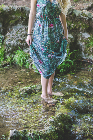 Close up on the legs of young woman wearing floral skirt barefoot in the riverの写真素材