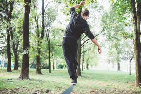 Man balancing a tightrope or slackline outdoor in a city park in autumn - slacklining, balance, training conceptの写真素材