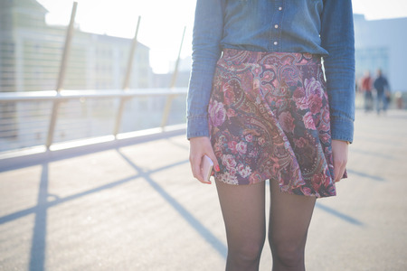 Young handsome caucasian girl posing in the street - detail of the dress composed by a floral skirt, a pair of black shoes and a jeans shirtの写真素材