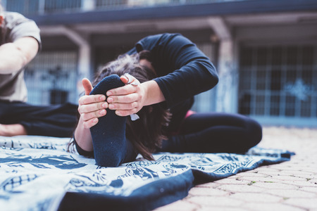Close up on the hand of young woman stretching outdoor in the city, holding her feet - training,...