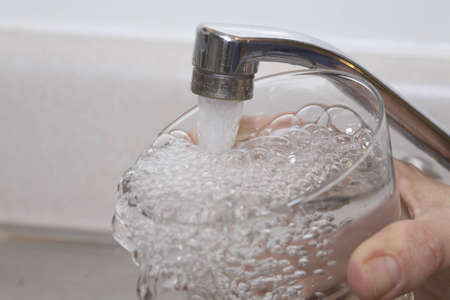 Overflowing glass of water under faucetの写真素材