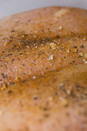 Raw chicken breast being prepared for cooking. Chicken is spiced with pepper, meat tenderizer, garlic, and ginger.の写真素材