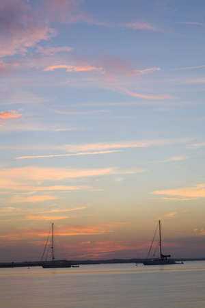 Sailboats anchored in harbor as the sun sets behind them. 