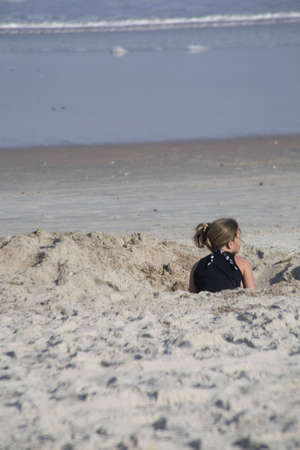 Female child playing in a hole in the sand at the beach. Oceanside fun by digging a hole in the sandの写真素材