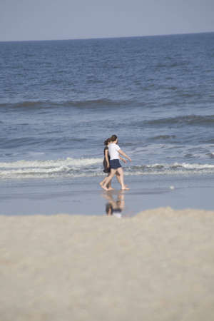 Three adult women walking on the beach in the surf barefoot.の写真素材