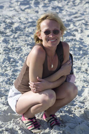 A mature adult woman at the beach in shorts, squatting in the sand.の写真素材