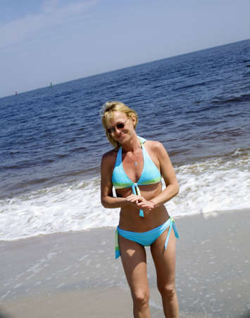Adult woman standing in the surf at the beach with her hands clasp in front of her. の写真素材
