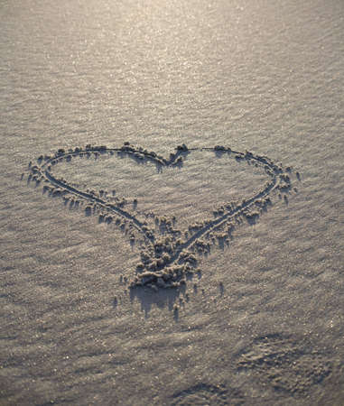 Heart symbol drawn into wet sand at the beach. Rising sun gives hand drawn heart a golden hue in the shoreline.の写真素材