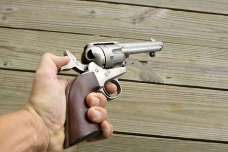 Cocked western style revolver being held in a hand pointed at a wallの写真素材