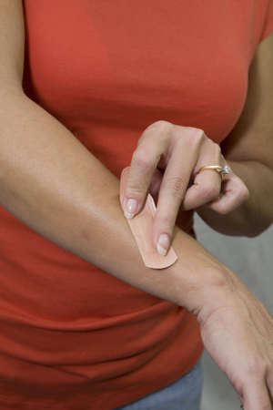 Close-up of a woman applying a bandage to her wounded arm. 