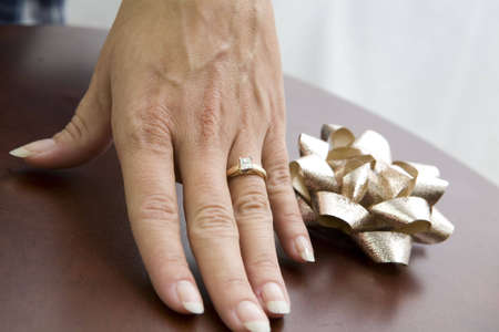 A woman showing off her new engagement ring next to a gift bow. 