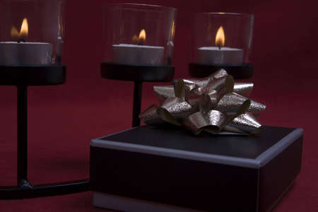 A small gift box set on a red background with a trio of candles softly lighting it. A romantic setting for giving a present suitable for any occasion.の写真素材