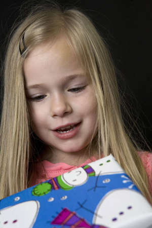 A young girl looking down at a large Christmas gift with a happy smile on her face.