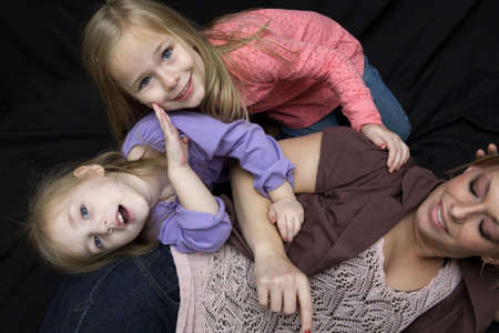 A mother and her daughters at playtime on the floor with the girls being silly. Looking down on the group on a black background.の写真素材