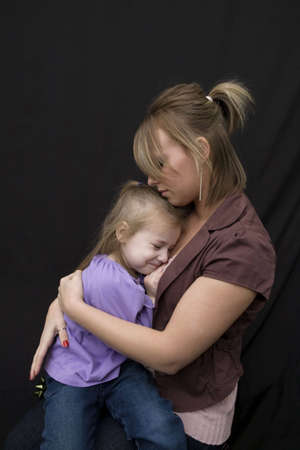 A young mother hugging her sad daughter. Shot from profile capturing the unhappy look on the little girls face.の写真素材