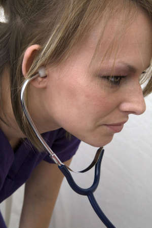 A female medical professional with stethoscope in her ears listening intently. の写真素材