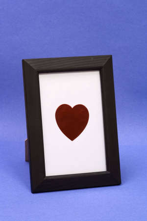 Heart symbol in a desk type picture frame shot on an angle. Isolated on blue background with white inside frame to isolate heart.の写真素材