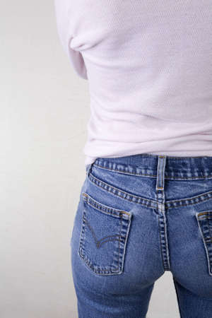 Rear shot of a woman in blue jeans and pink shirt. Left side of female body from the rear with her arms crossed out of view. Copy space to the left of the frame.の写真素材