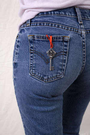 A symbolic skeleton key on a red romantic ribbon hanging from the rear pocket of her pants. の写真素材