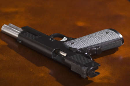 A 1911 model 45 caliber pistol on a bright cherry desk with slide open. Shot in low depth of field with stark lighting to create an ominous atmosphere.の写真素材