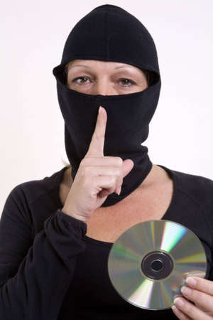 Woman thief stealing data on a cd, holding her finger to her mouth for silence. の写真素材