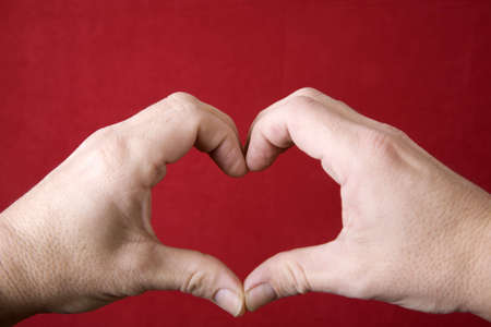 A heart symbol made with hands on a red background. の写真素材