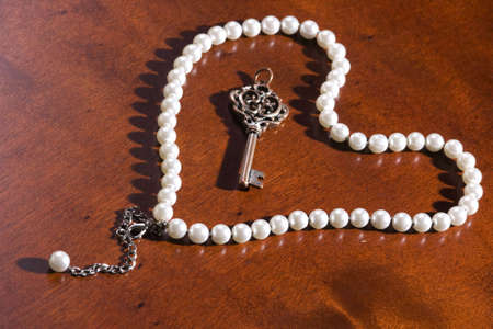 Key with a pearl necklace, as the concept that jewelry is the key to her heart on special days. High key shot with sharp shadows of pearls on a wooden backgroundの写真素材