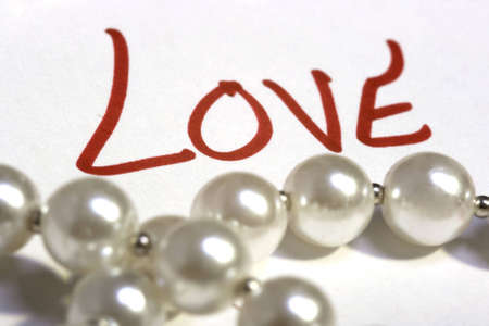 The word love in focus behind a string of pearls.の写真素材