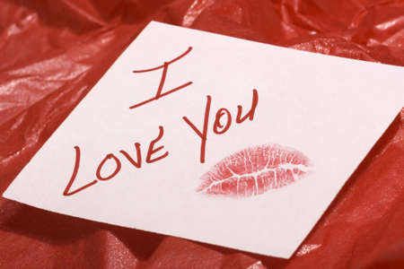 A love note, sealed with a lipstick kiss, on white paper over red crinkled gift wrap paperの写真素材