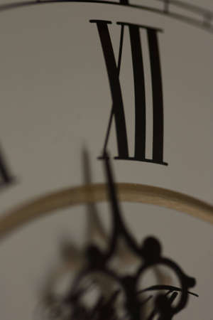 A dark image of a clock arm striking midnight, concept of a new start or year. Shallow depth of field creating a grainy dreamy look invoking the concept of looking at the clock late at night and an appearance of motion to the hour hand.の写真素材