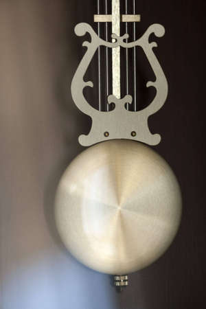 A clock pendulum with musical harp design caught in bright reflecting lightの写真素材