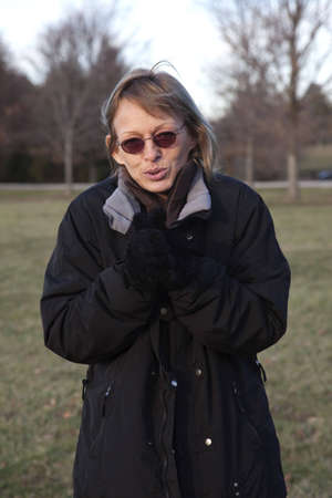 A woman in coat and gloves, shivering in the cold. Female bracing against the cold of winter on a day at the park.の写真素材