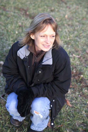 A woman squatting down in a grass field on a suny winter day.の写真素材