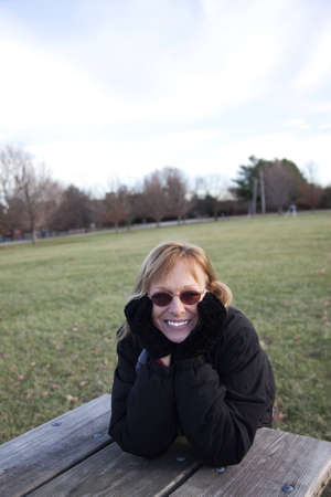 A woman leaning on a picnic bench at a park  with her head in her hands showing interest as she watches. の写真素材