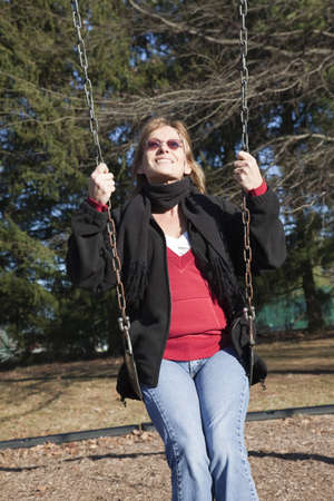Adult woman looking up in setting winter sun as she swings on a swingset.の写真素材