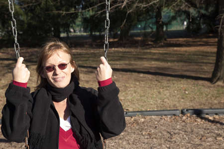 Adult woman swinging in the setting sun on a winter outing to the park. の写真素材