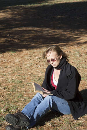 A woman sitting in a grass field enjoying reading a book. の写真素材
